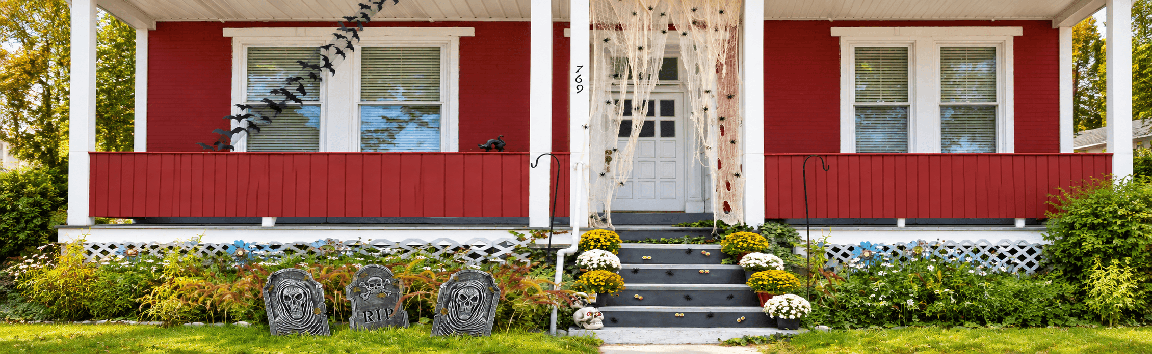 A red house, dressed with hanging bat décor, spiderwebs, spiders, flowerpots, and stairs covered with eyeballs